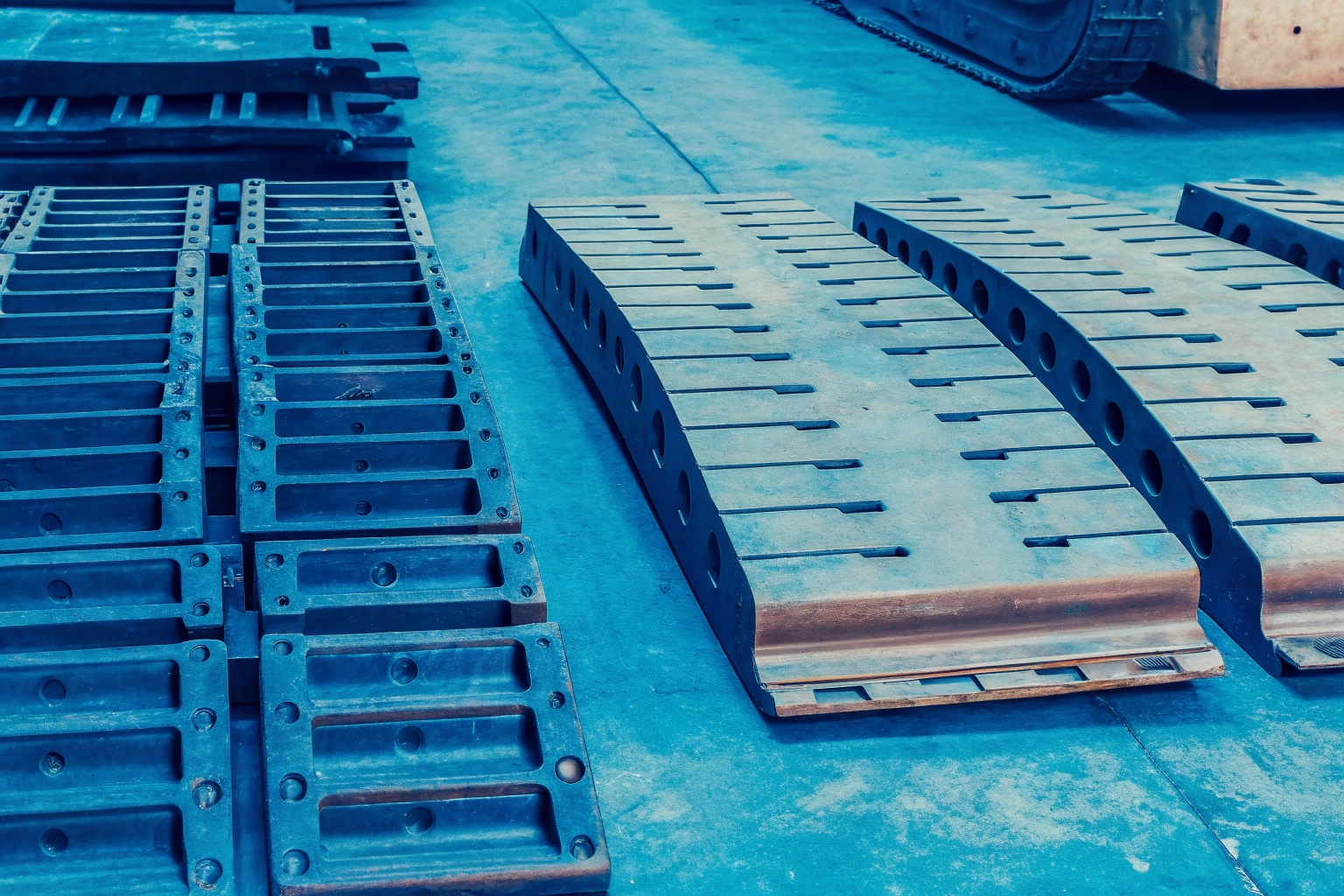 New steel track pads for heavy machinery undercarriages laid out on a factory floor.