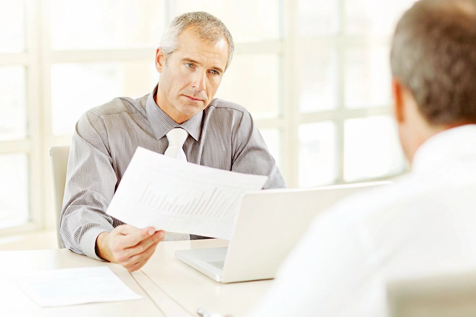 Businessman in meeting reviewing a technical document with charts at his laptop.