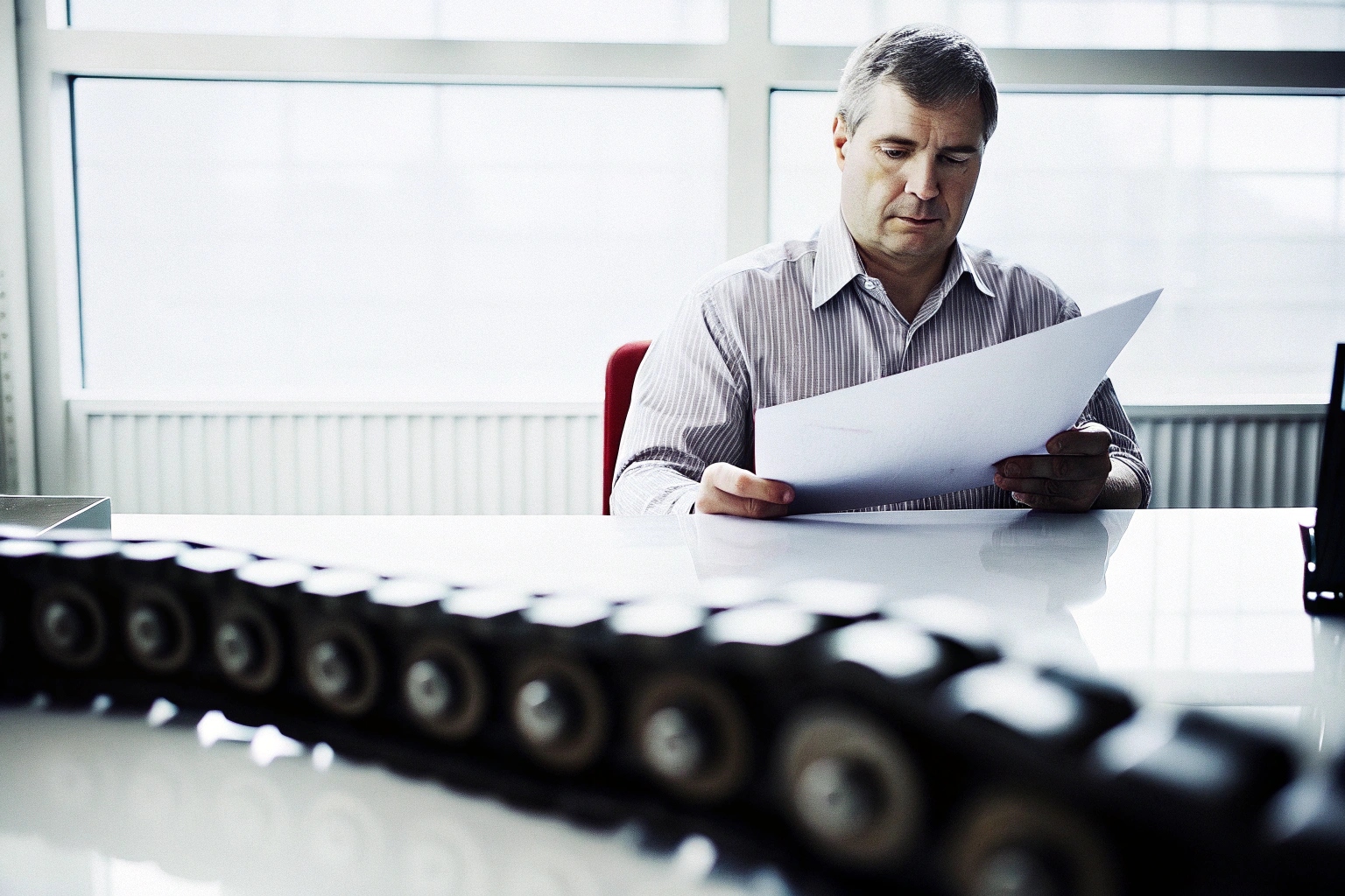 Engineer reviewing technical documents at a desk with a conveyor chain in the foreground.