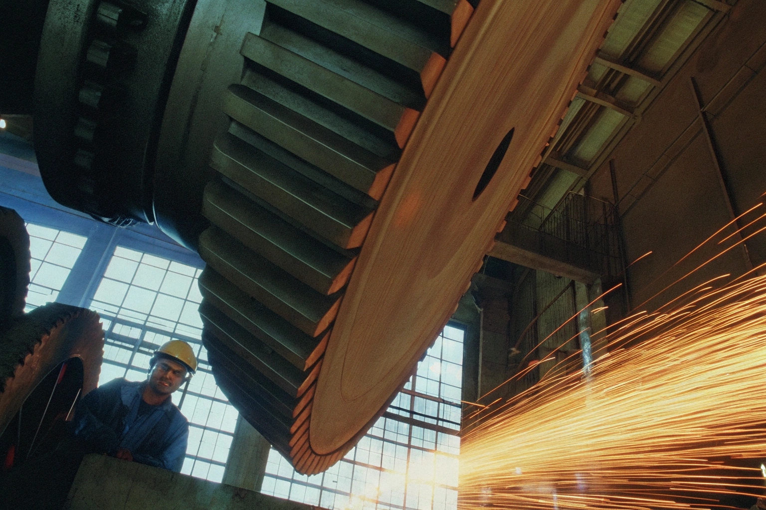Worker observing manufacturing of a large industrial gear with sparks flying from welding.