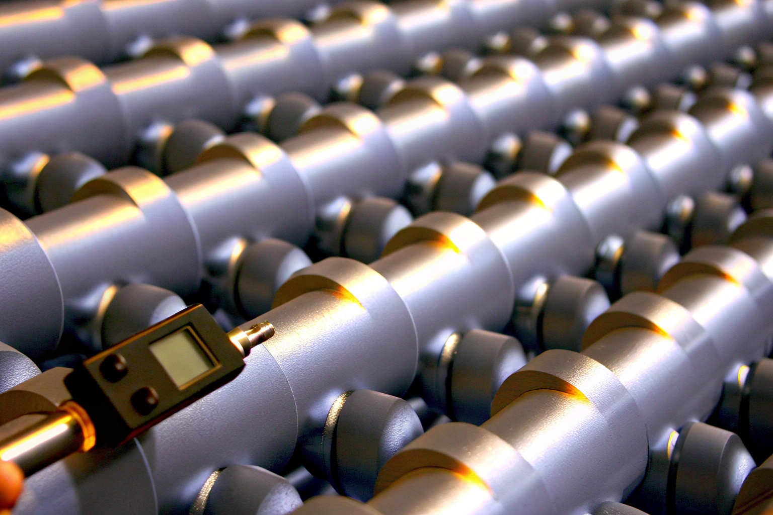 Digital gauge performing quality control inspection on rows of machined metal parts.