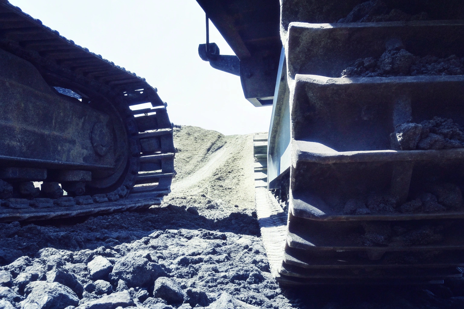 Low-angle view between the tracks of two heavy-duty construction vehicles on site.